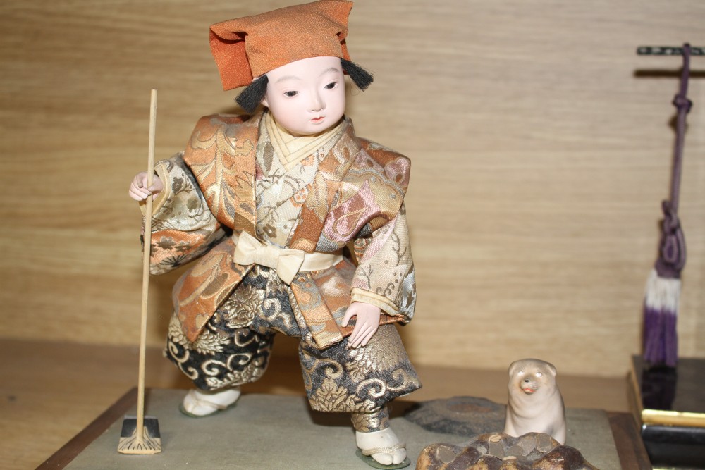 A Japanese late Meiji period composition and fabric figure of a boy farmer holding an adze with puppy seated nearby, mounted on display